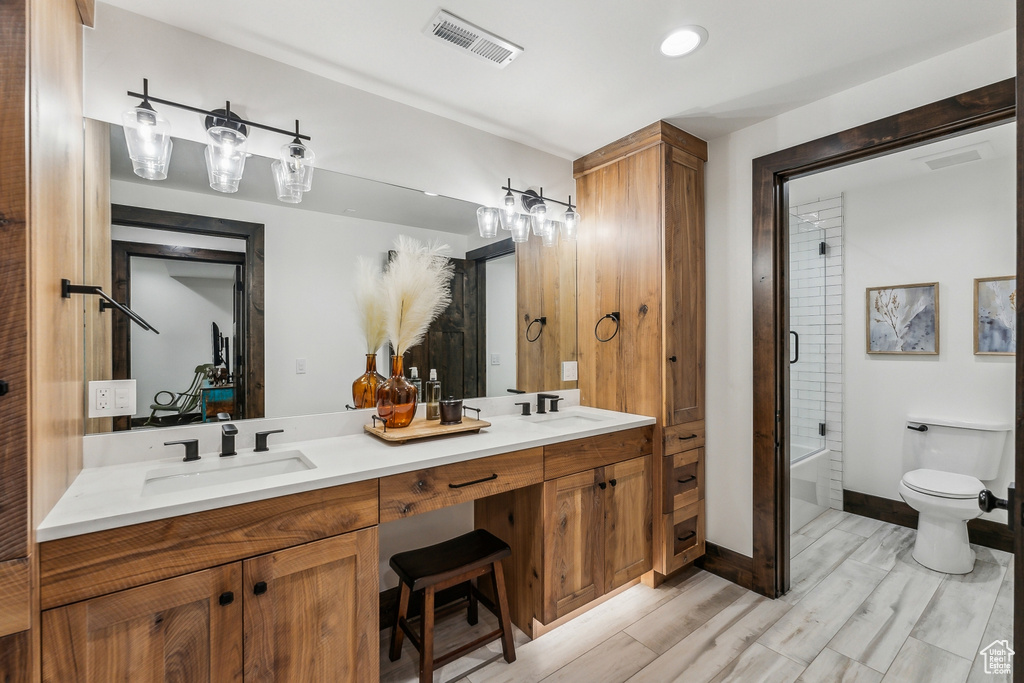 Full bathroom featuring dual vanity, enclosed tub / shower combo, toilet, and hardwood / wood-style flooring