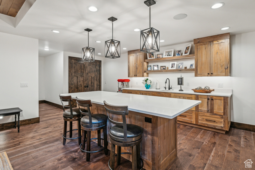 Kitchen with a kitchen breakfast bar, dark hardwood / wood-style flooring, pendant lighting, a center island, and sink