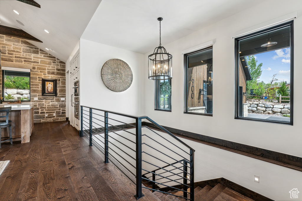 Hall with vaulted ceiling, plenty of natural light, dark hardwood / wood-style floors, and an inviting chandelier