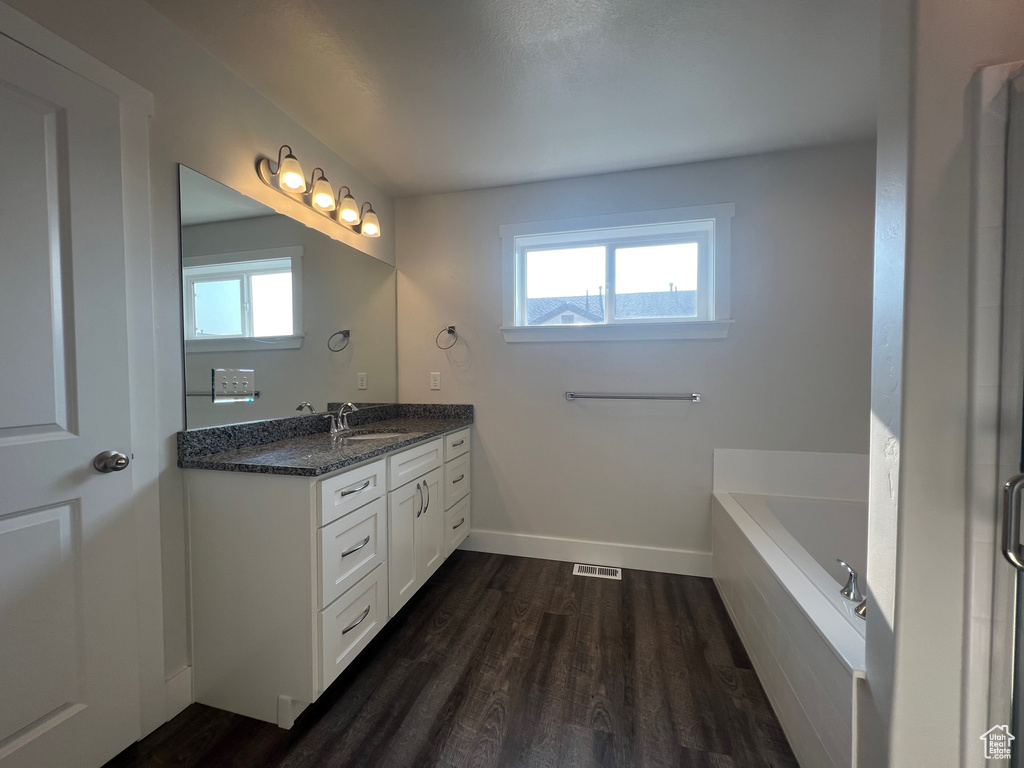 Bathroom with plenty of natural light, vanity, a relaxing tiled tub, and hardwood / wood-style floors