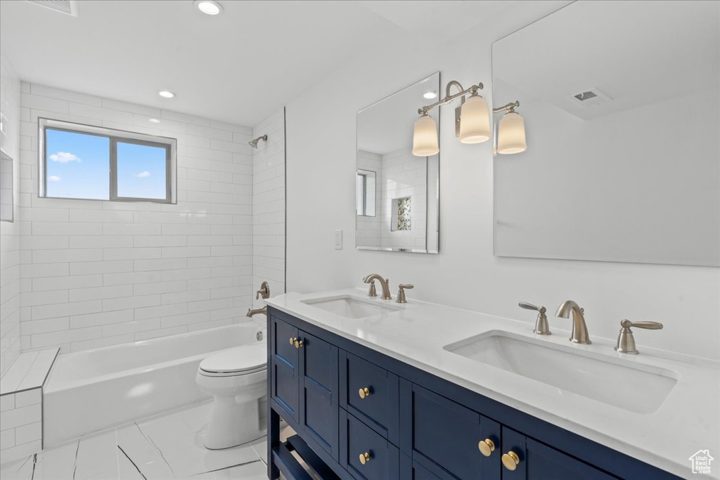 Full bathroom featuring tiled shower / bath combo, double sink vanity, toilet, and tile patterned flooring