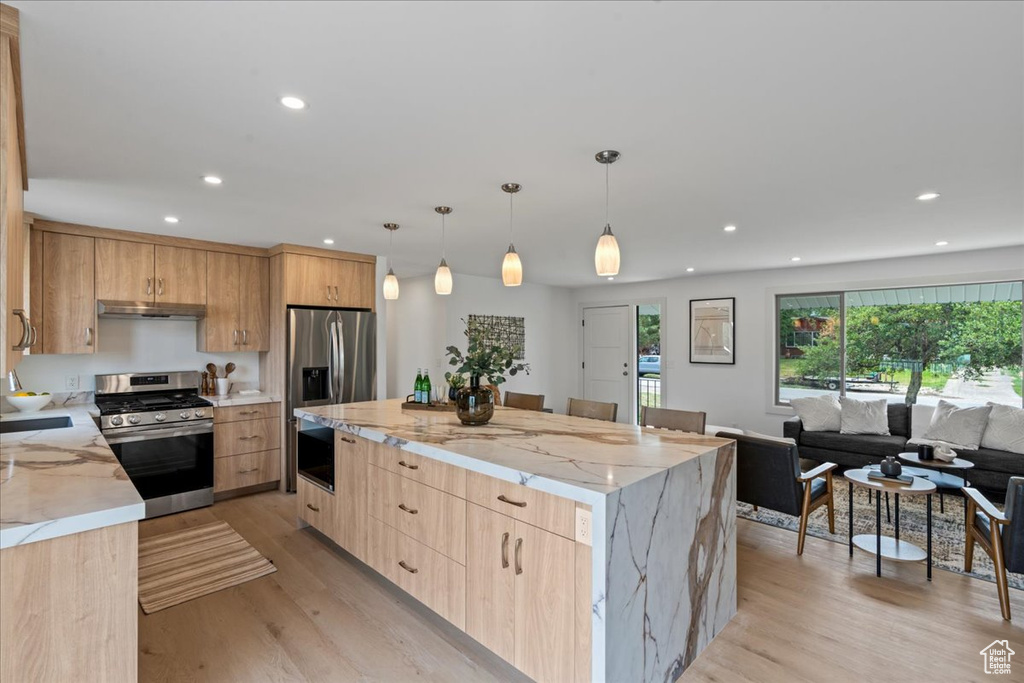 Kitchen featuring light hardwood / wood-style flooring, light brown cabinetry, appliances with stainless steel finishes, light stone countertops, and a center island