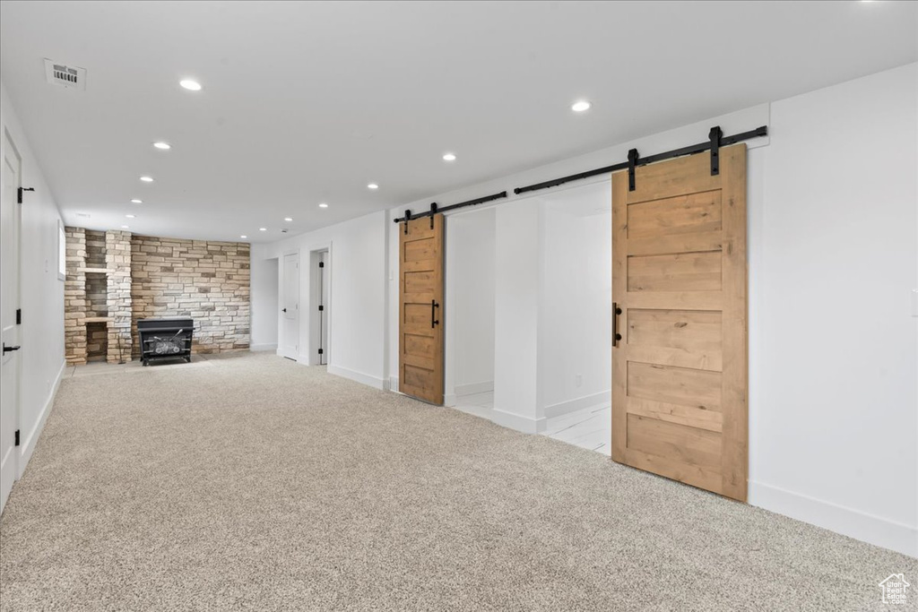 Unfurnished living room featuring a barn door, light colored carpet, and a large fireplace