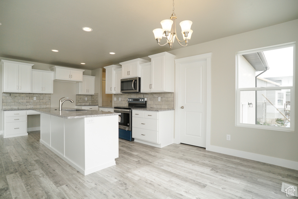 Kitchen featuring appliances with stainless steel finishes, light hardwood / wood-style flooring, decorative backsplash, and white cabinetry