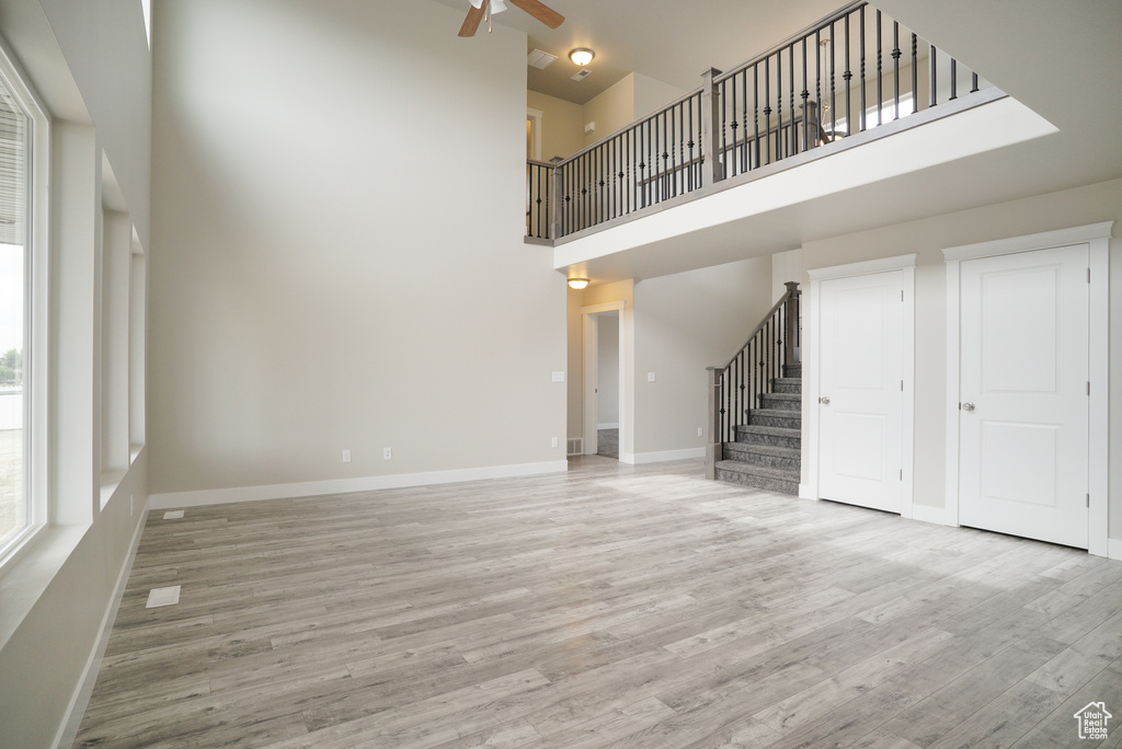 Unfurnished living room featuring a towering ceiling, hardwood / wood-style floors, and ceiling fan