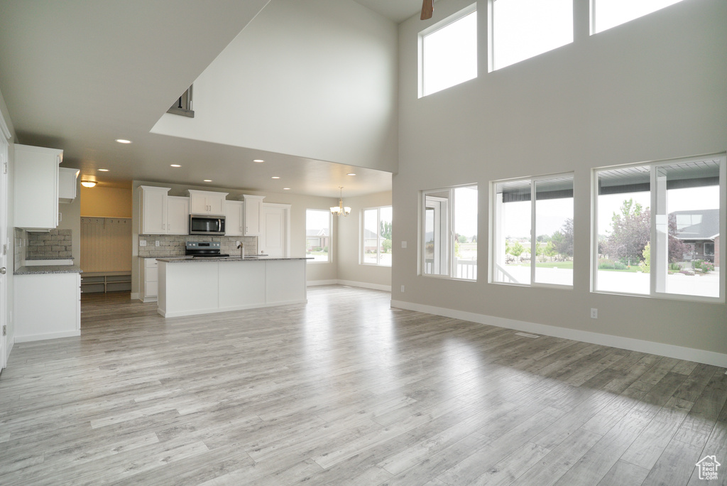 Unfurnished living room with an inviting chandelier, sink, a high ceiling, and light hardwood / wood-style floors