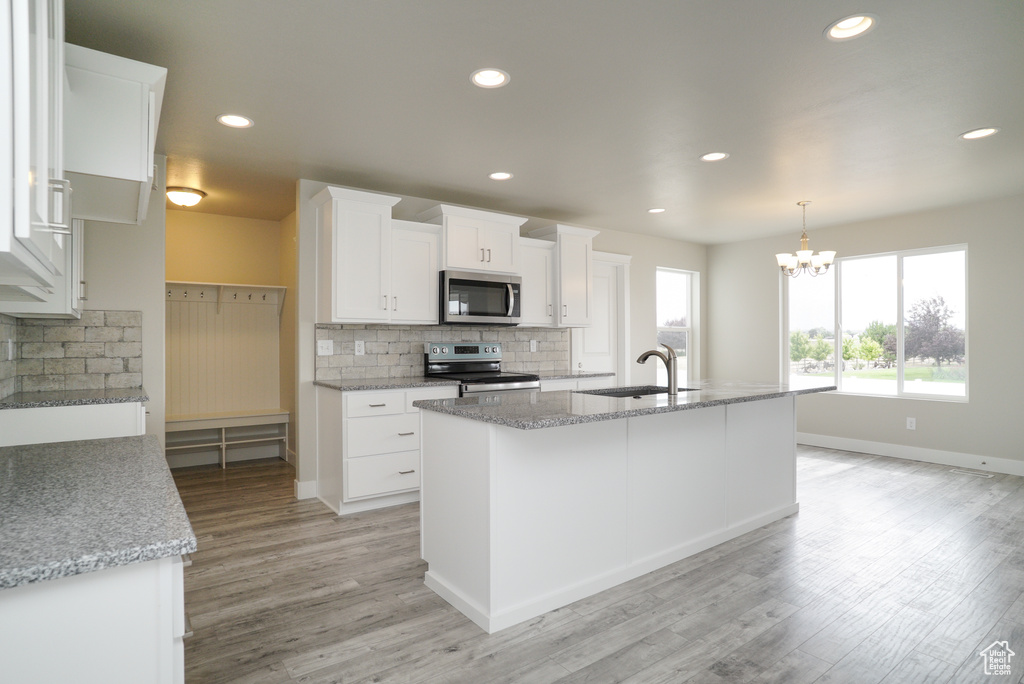 Kitchen featuring tasteful backsplash, appliances with stainless steel finishes, an island with sink, white cabinetry, and light hardwood / wood-style flooring