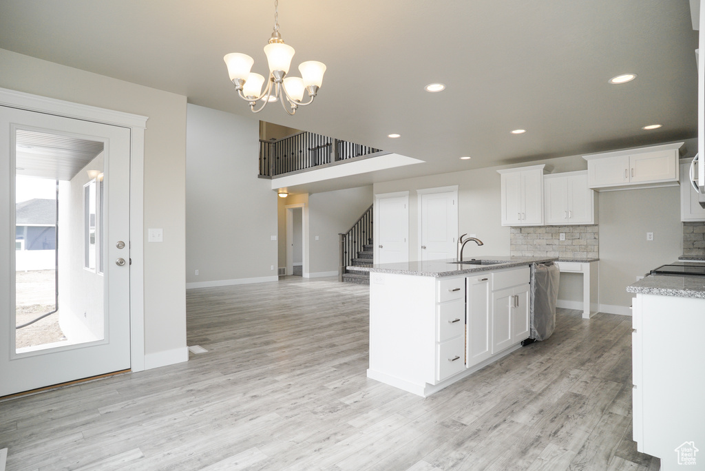 Kitchen with white cabinets, a kitchen island with sink, light wood-type flooring, and tasteful backsplash