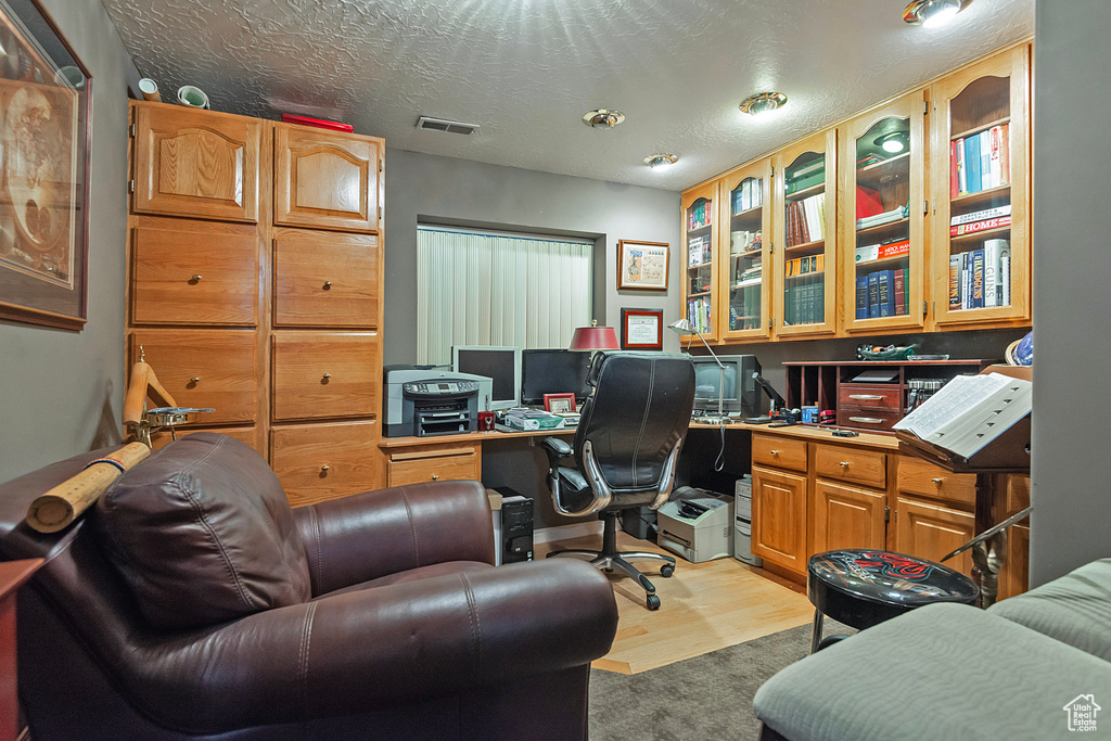 Office space featuring a textured ceiling, light hardwood / wood-style flooring, and built in desk