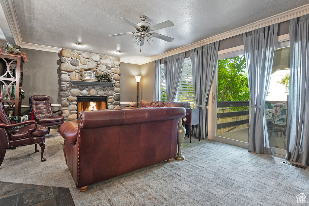 Carpeted living room featuring a textured ceiling, a fireplace, ceiling fan, and crown molding