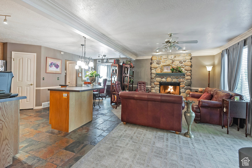 Living room with a stone fireplace, a textured ceiling, ceiling fan with notable chandelier, and a healthy amount of sunlight