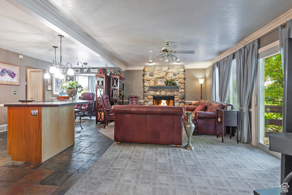 Living room with a textured ceiling, ceiling fan with notable chandelier, carpet floors, a fireplace, and ornamental molding