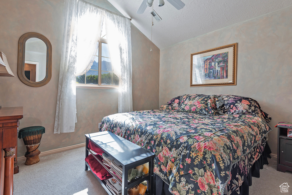 Bedroom with lofted ceiling, a textured ceiling, light colored carpet, and ceiling fan