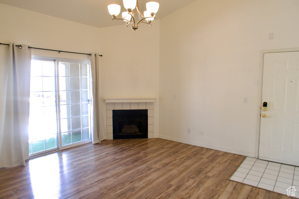 Unfurnished living room with wood-type flooring, a chandelier, and a tile fireplace