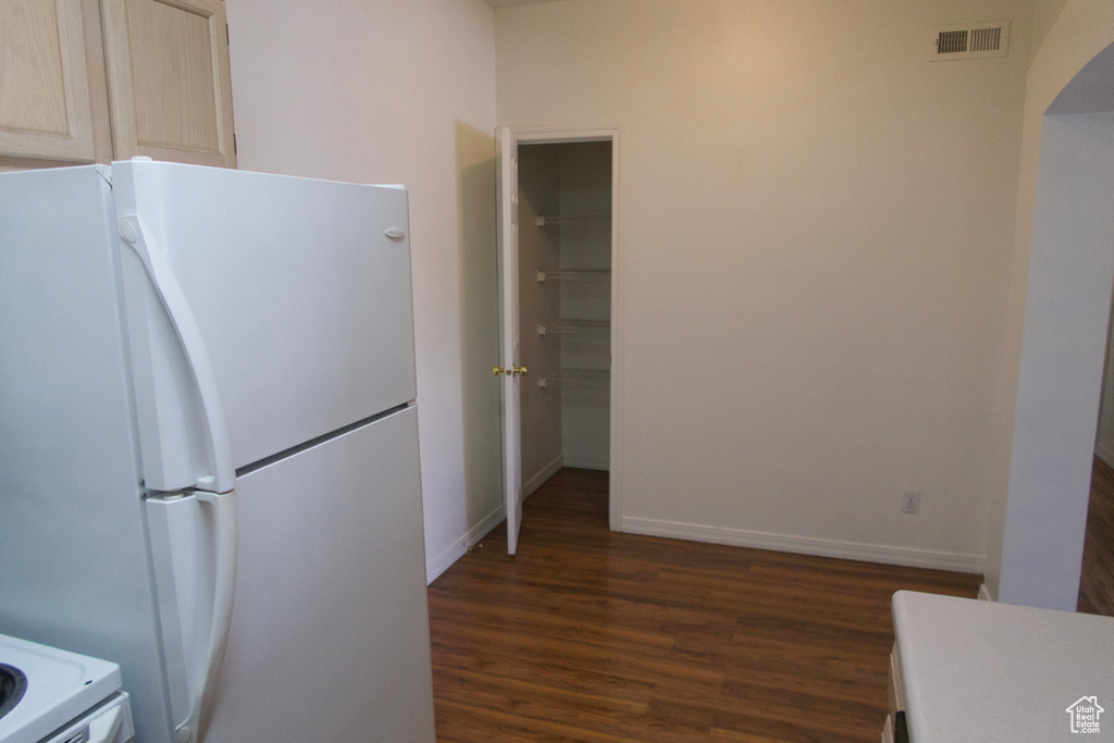 Kitchen with white refrigerator, dark wood-type flooring, and light brown cabinets