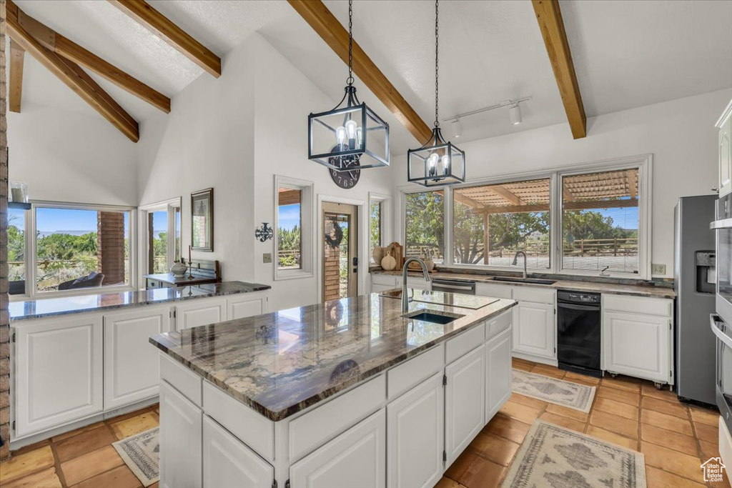 Kitchen featuring beamed ceiling, white cabinetry, and a center island with sink