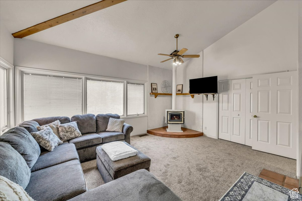 Carpeted living room with beam ceiling, ceiling fan, high vaulted ceiling, and a wood stove