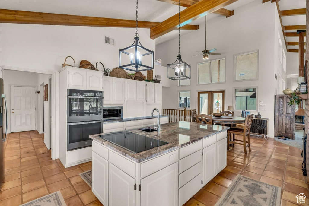 Kitchen with dark stone countertops, a kitchen island with sink, stainless steel appliances, and white cabinetry