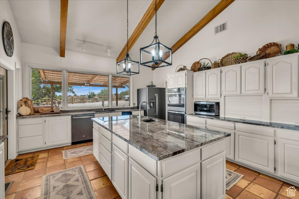 Kitchen with beam ceiling, appliances with stainless steel finishes, an island with sink, and white cabinetry
