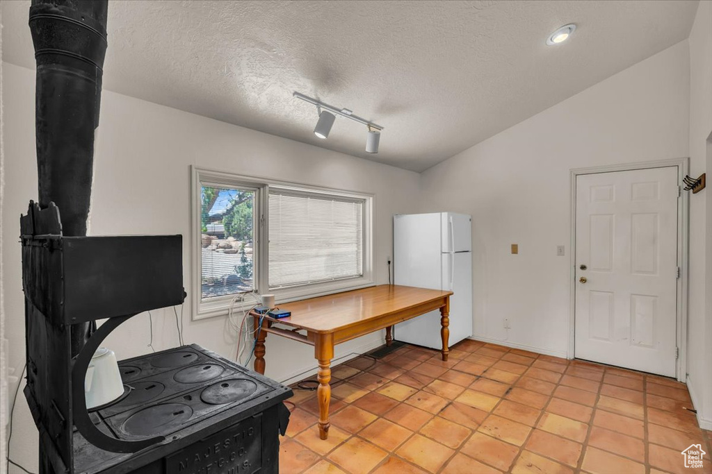 Office area with a textured ceiling, light tile patterned floors, vaulted ceiling, a wood stove, and track lighting