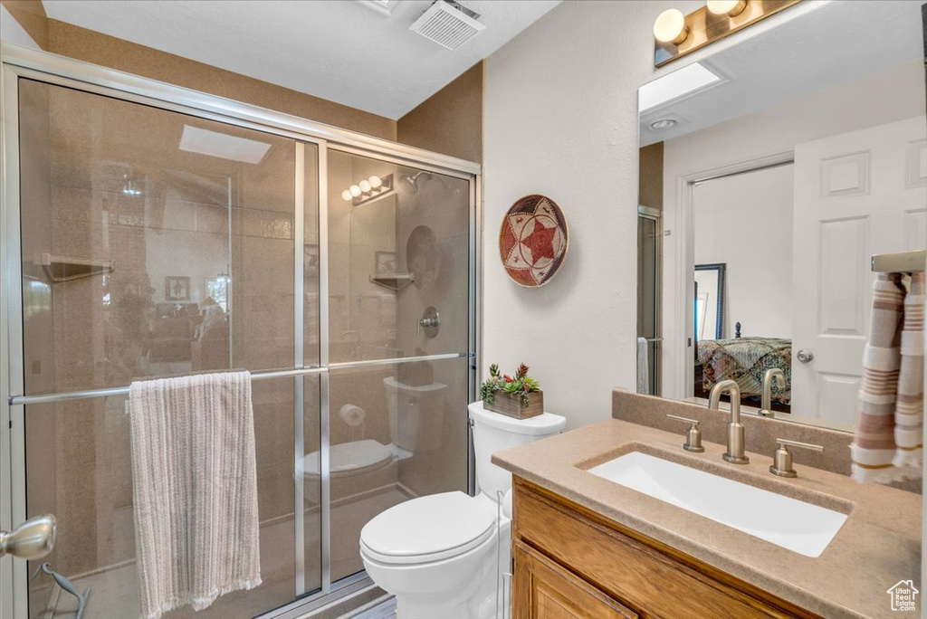 Bathroom with a shower with shower door, vanity, and toilet