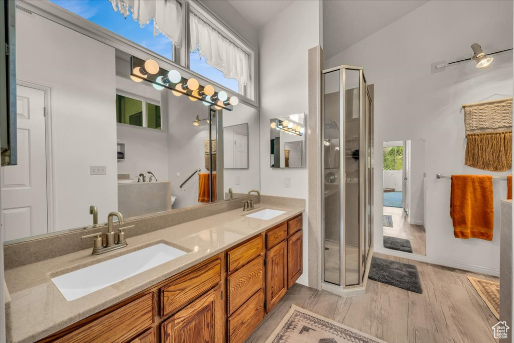Bathroom featuring dual bowl vanity, high vaulted ceiling, wood-type flooring, a shower with shower door, and ceiling fan