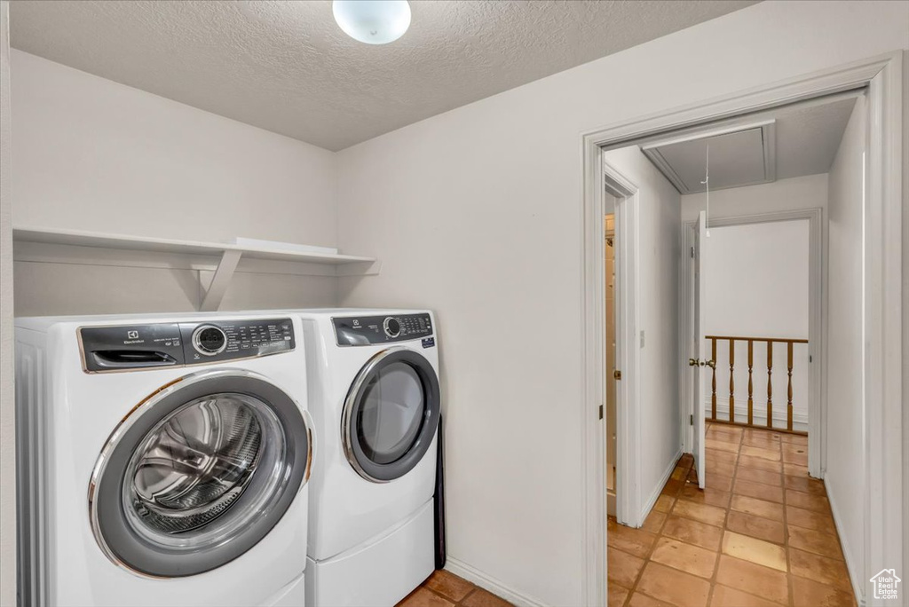 Clothes washing area with light tile patterned flooring, washing machine and dryer, and a textured ceiling