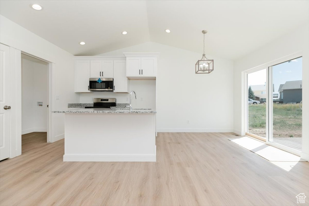 Kitchen featuring vaulted ceiling, light stone countertops, light hardwood / wood-style flooring, stove, and white cabinetry