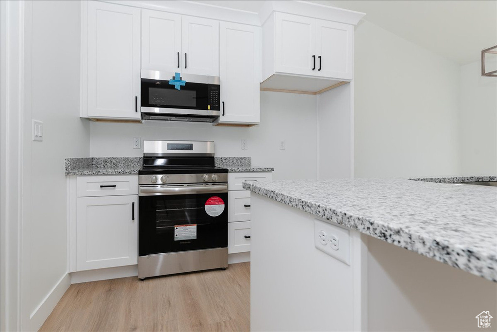 Kitchen with white cabinetry, light hardwood / wood-style flooring, stainless steel appliances, and light stone countertops