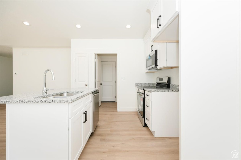 Kitchen with light wood-type flooring, stainless steel appliances, sink, light stone countertops, and a center island with sink