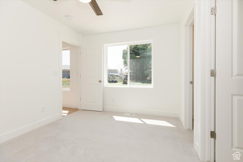 Carpeted empty room featuring a healthy amount of sunlight and ceiling fan