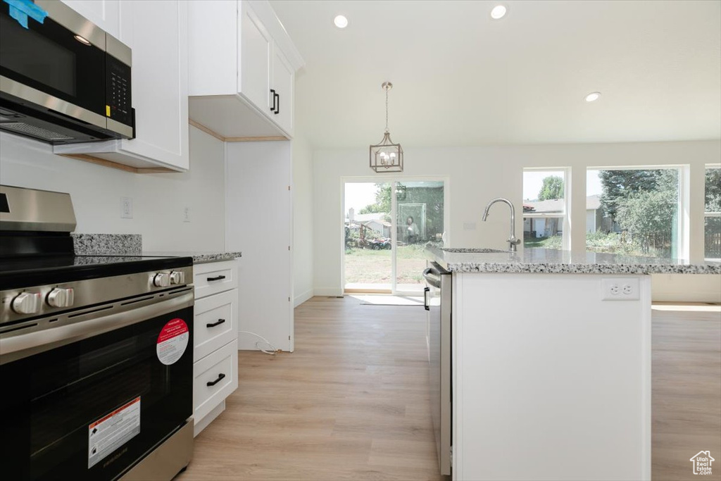 Kitchen with appliances with stainless steel finishes, plenty of natural light, a center island with sink, and light hardwood / wood-style floors