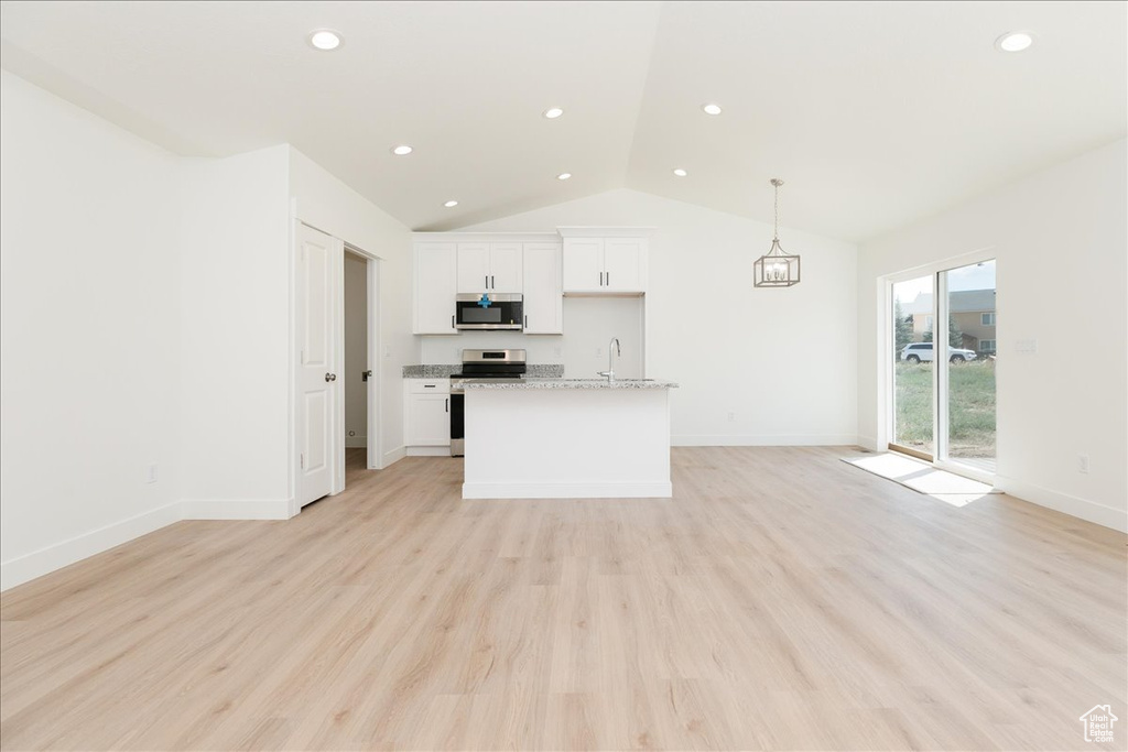 Kitchen with light wood-type flooring, appliances with stainless steel finishes, light stone countertops, white cabinetry, and lofted ceiling