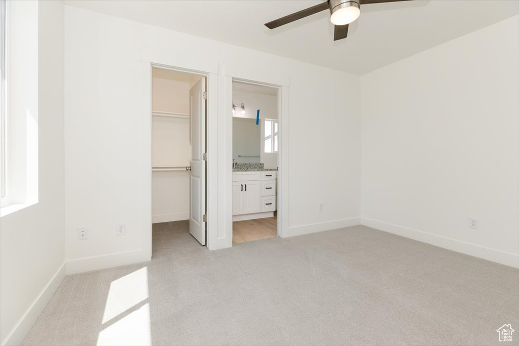 Unfurnished bedroom featuring a spacious closet, a closet, ensuite bath, light colored carpet, and ceiling fan