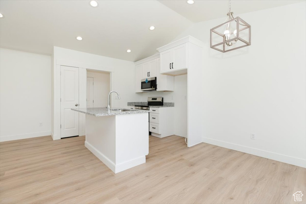 Kitchen with stove, light hardwood / wood-style flooring, light stone counters, and a center island with sink