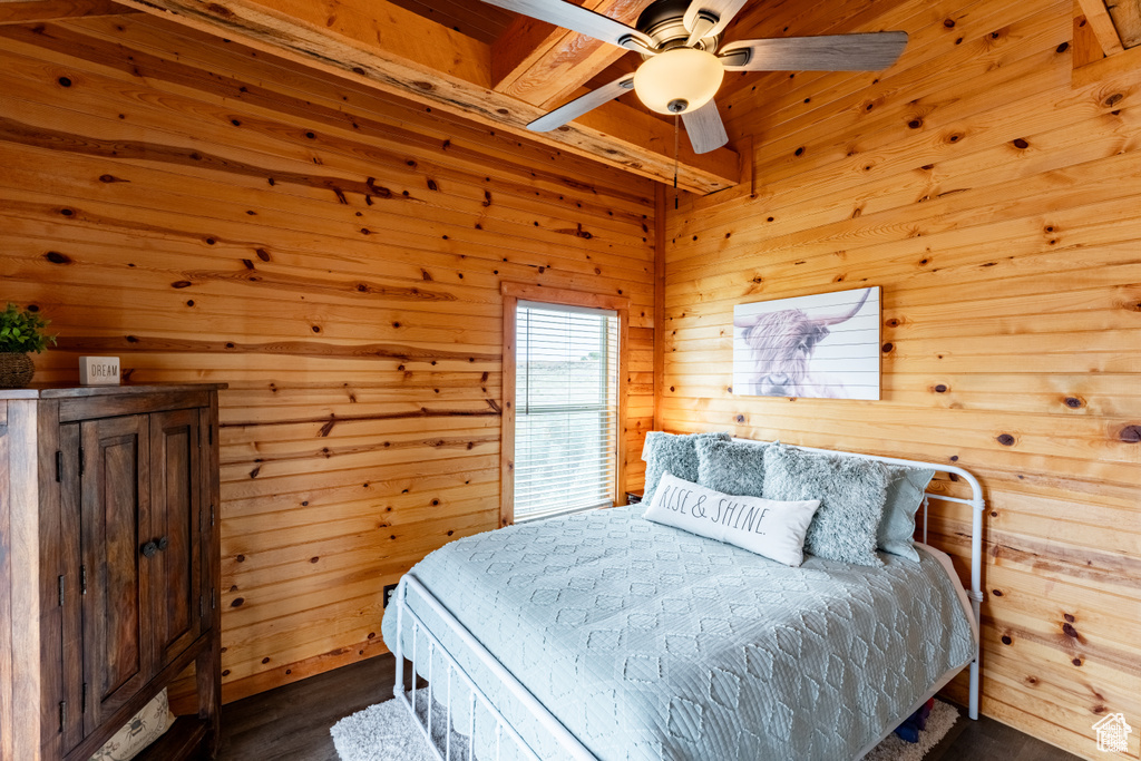 Bedroom featuring beamed ceiling, ceiling fan, wooden walls, and hardwood / wood-style floors