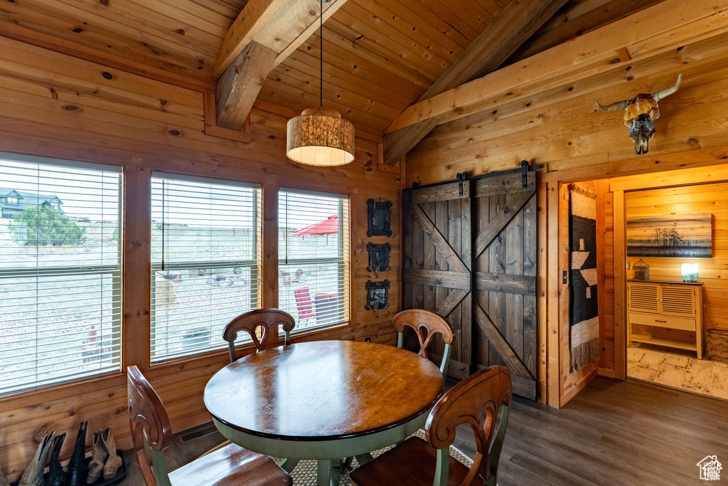 Dining space featuring a barn door, hardwood / wood-style floors, wooden walls, vaulted ceiling, and wooden ceiling