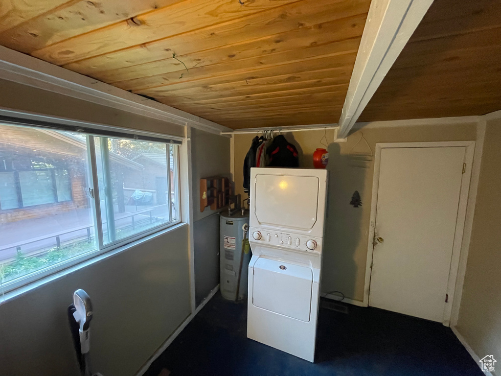 Laundry area featuring wooden ceiling, stacked washing maching and dryer, electric water heater, and a wealth of natural light