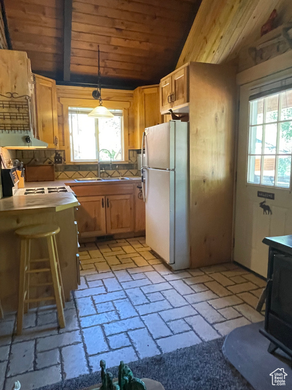 Kitchen with a wealth of natural light, lofted ceiling, white refrigerator, and hanging light fixtures