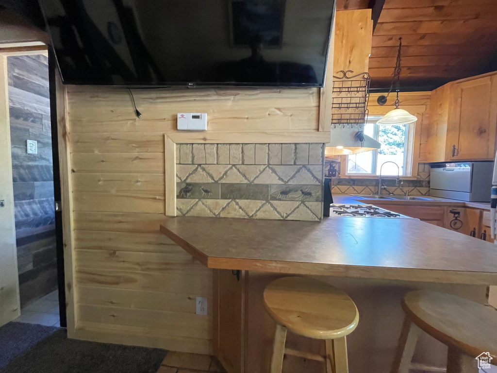 Kitchen with pendant lighting, wood walls, sink, wooden ceiling, and a kitchen bar