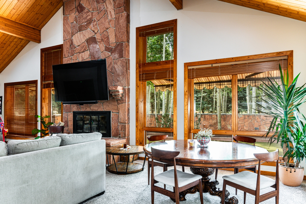 Carpeted dining area with high vaulted ceiling, a fireplace, beamed ceiling, and wooden ceiling