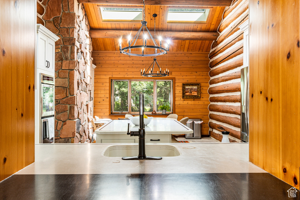 Unfurnished dining area featuring vaulted ceiling with skylight, wooden walls, sink, log walls, and wooden ceiling