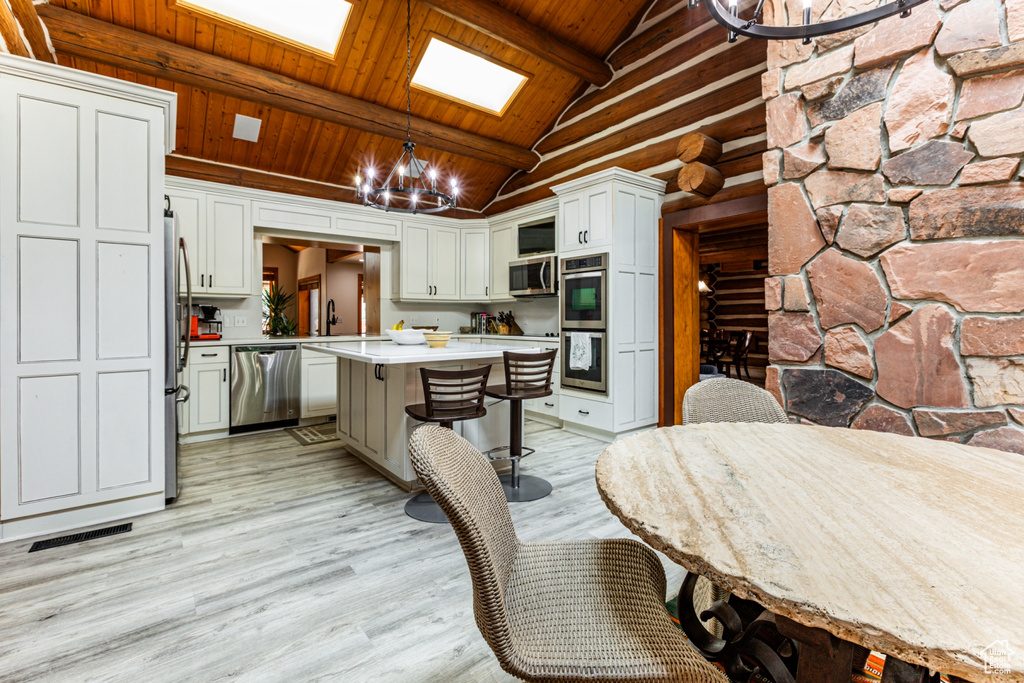 Dining area with light wood-type flooring, wooden ceiling, a chandelier, sink, and lofted ceiling with beams