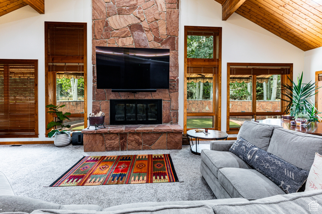 Carpeted living room with wooden ceiling, beamed ceiling, a stone fireplace, and high vaulted ceiling