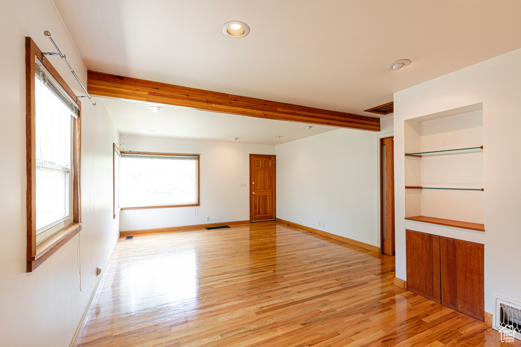 Spare room featuring beamed ceiling, light wood-type flooring, and built in features