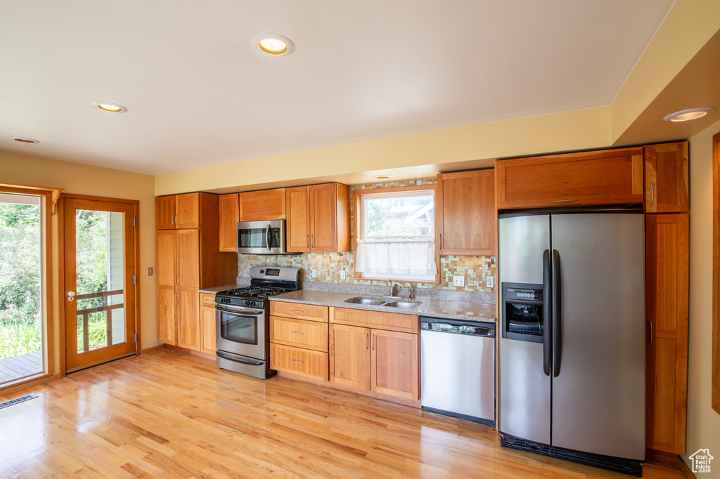 Kitchen with appliances with stainless steel finishes, sink, light hardwood / wood-style flooring, and decorative backsplash