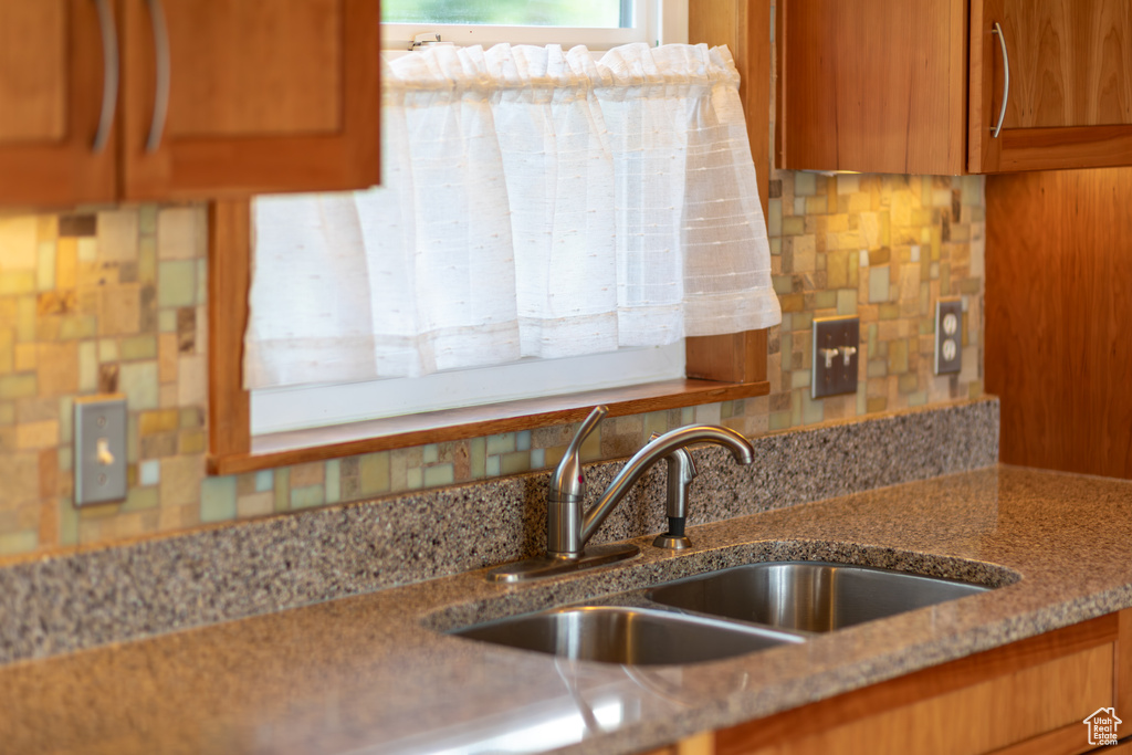 Kitchen featuring decorative backsplash, light stone counters, and sink