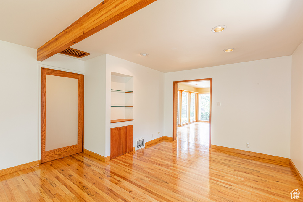 Empty room featuring beamed ceiling, light wood-type flooring, and built in features