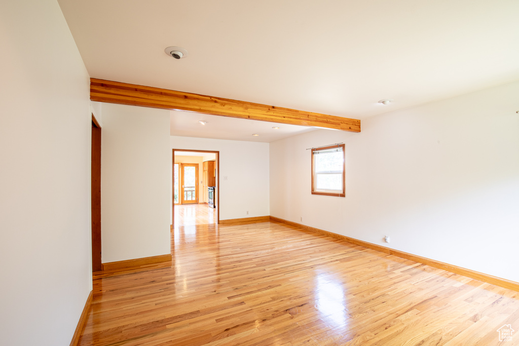 Empty room with light hardwood / wood-style flooring and beam ceiling