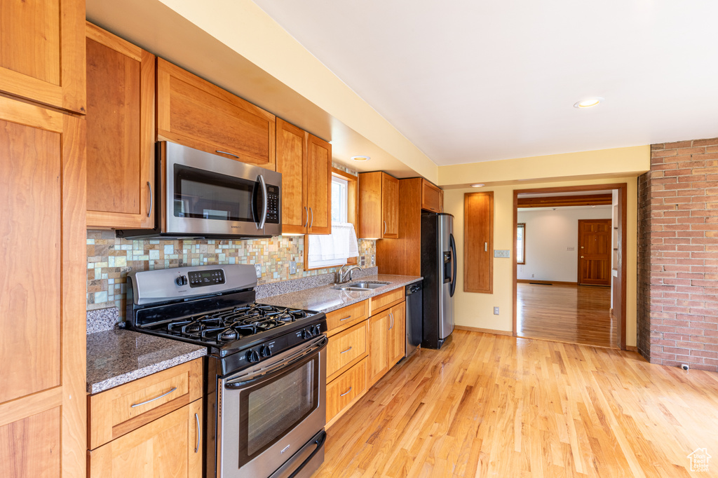 Kitchen with stainless steel appliances, dark stone countertops, light hardwood / wood-style floors, backsplash, and brick wall